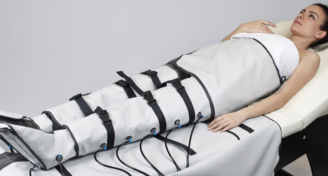 Kundin liegt mit angelegten Kompressionsmanschetten an Beinen und Bauch während der Pressotherapie